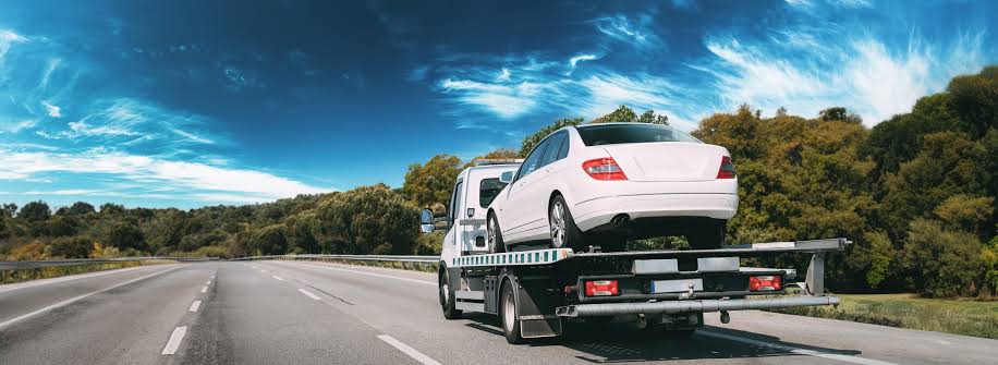 Flatbed tow truck transporting a damaged car safely